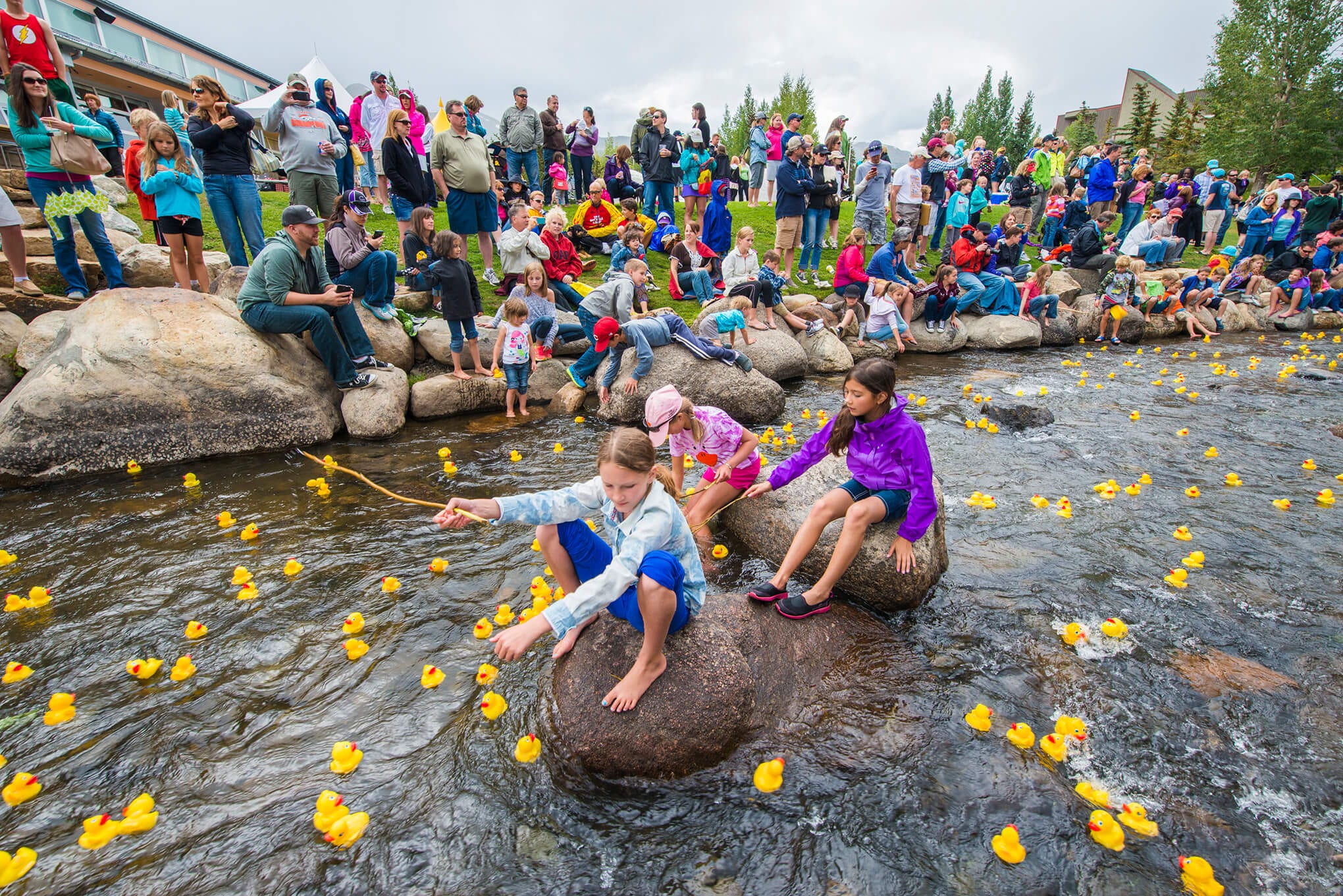 Kids sitting on rocks during the Labor Day Duck Race taking place on the Blue River in Breckenridge.
