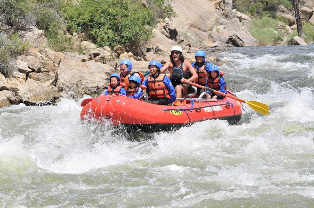 A family smiling on a raft going through rapids in the Brown Canyon in Colorado.