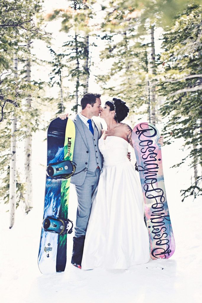 Newlyweds kissing in trees in Breckenridge with snowboards
