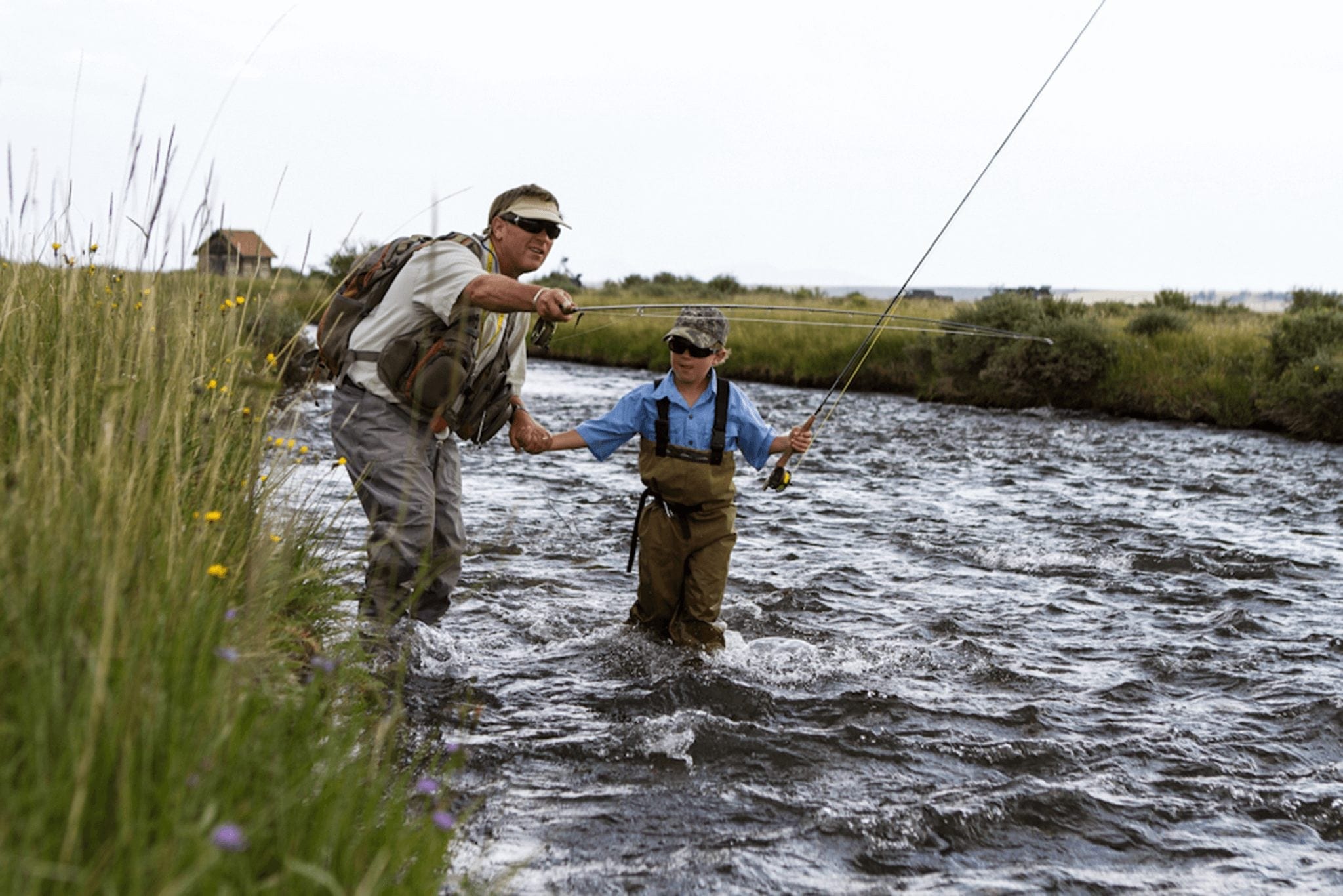 A father holds his son's hand while teaching him to fly fish in Breckenridge.