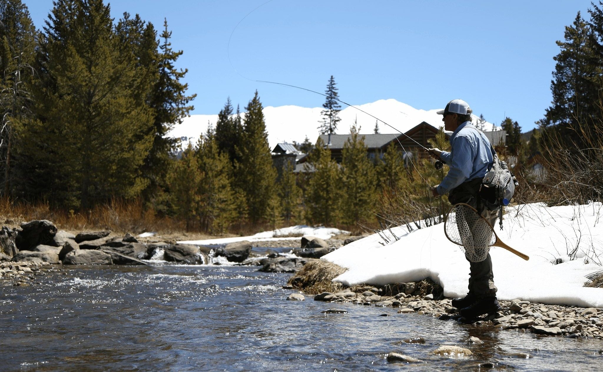A man casting while fly fishing with snow on the ground in Breckenridge.