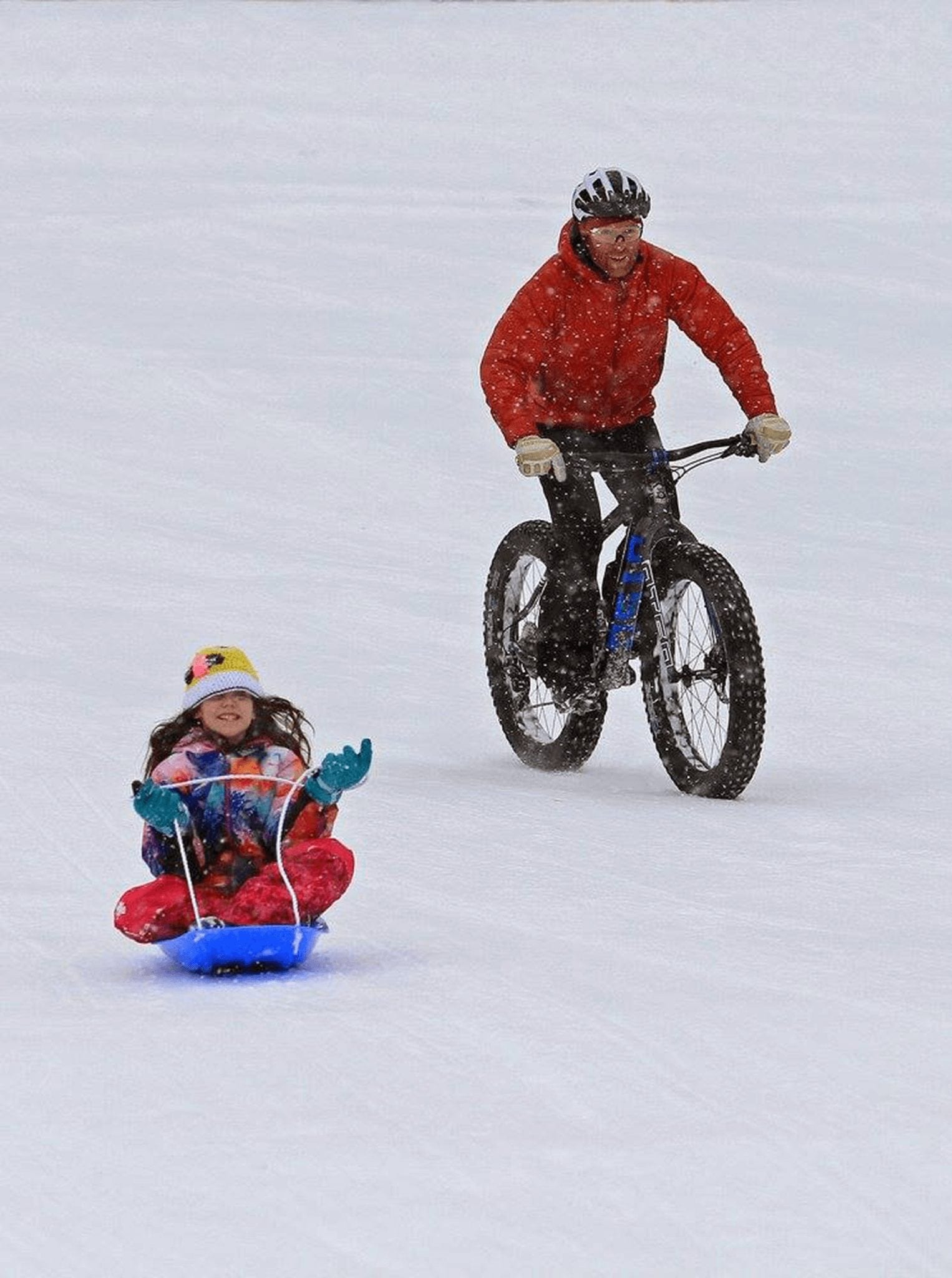 Father fat tire biking while daughter slides down hill in a sled in Breckenridge.