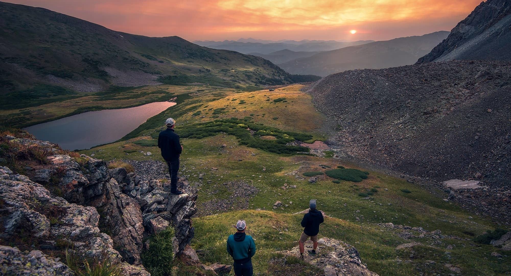 Three guys watch a sunset in the mountains while hiking
