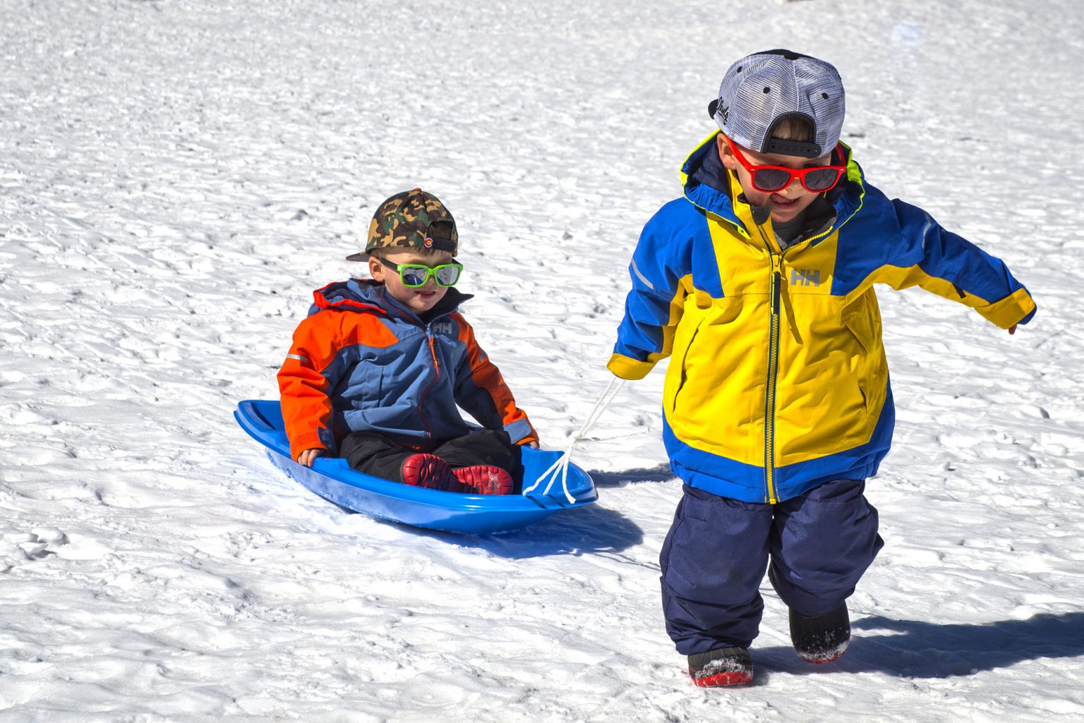 A young boy pulling his friend on a sled over the snow