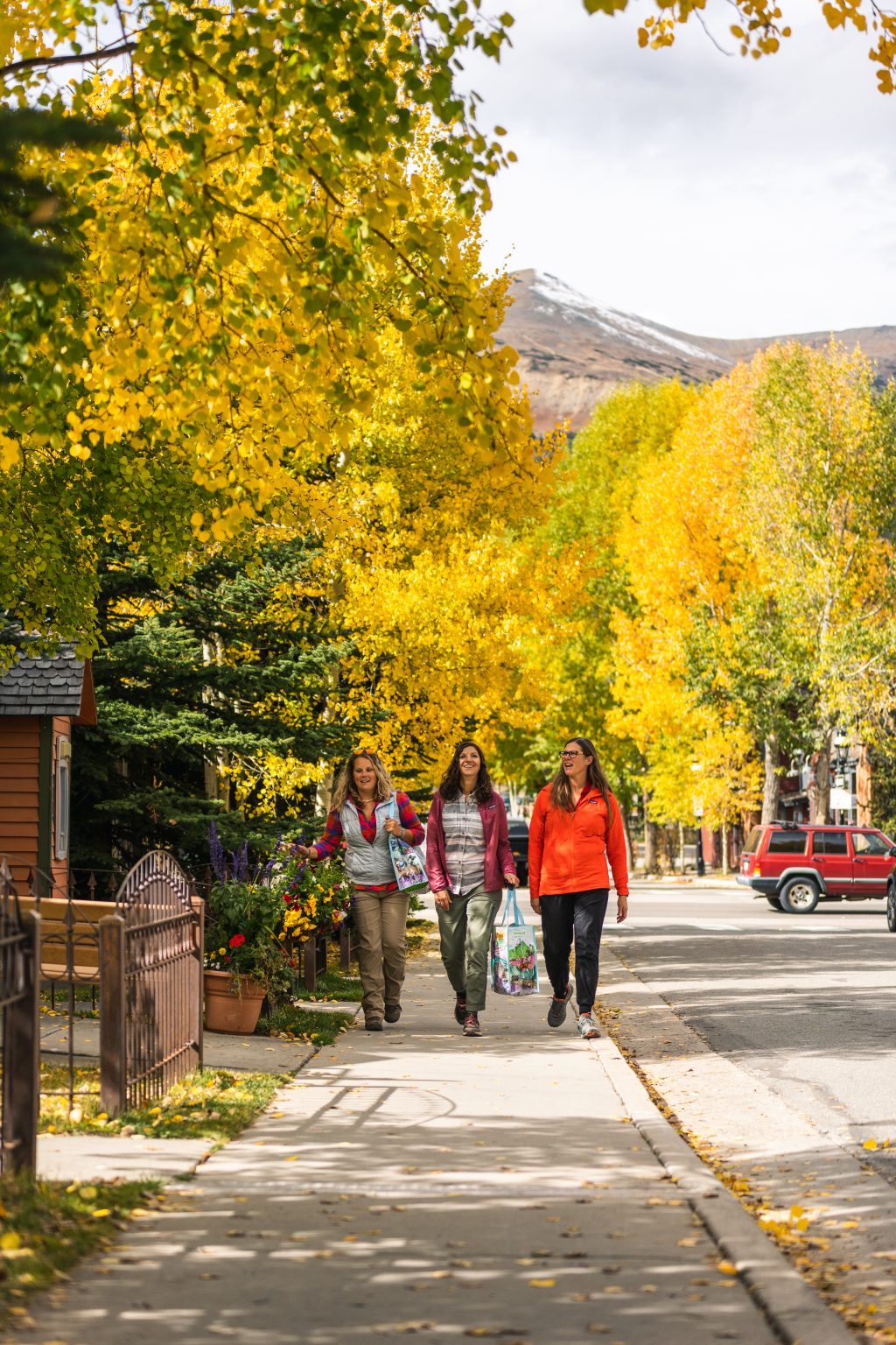 Three friends strolling along a sidewalk in Breckenridge with fall colors bursting alongside them.