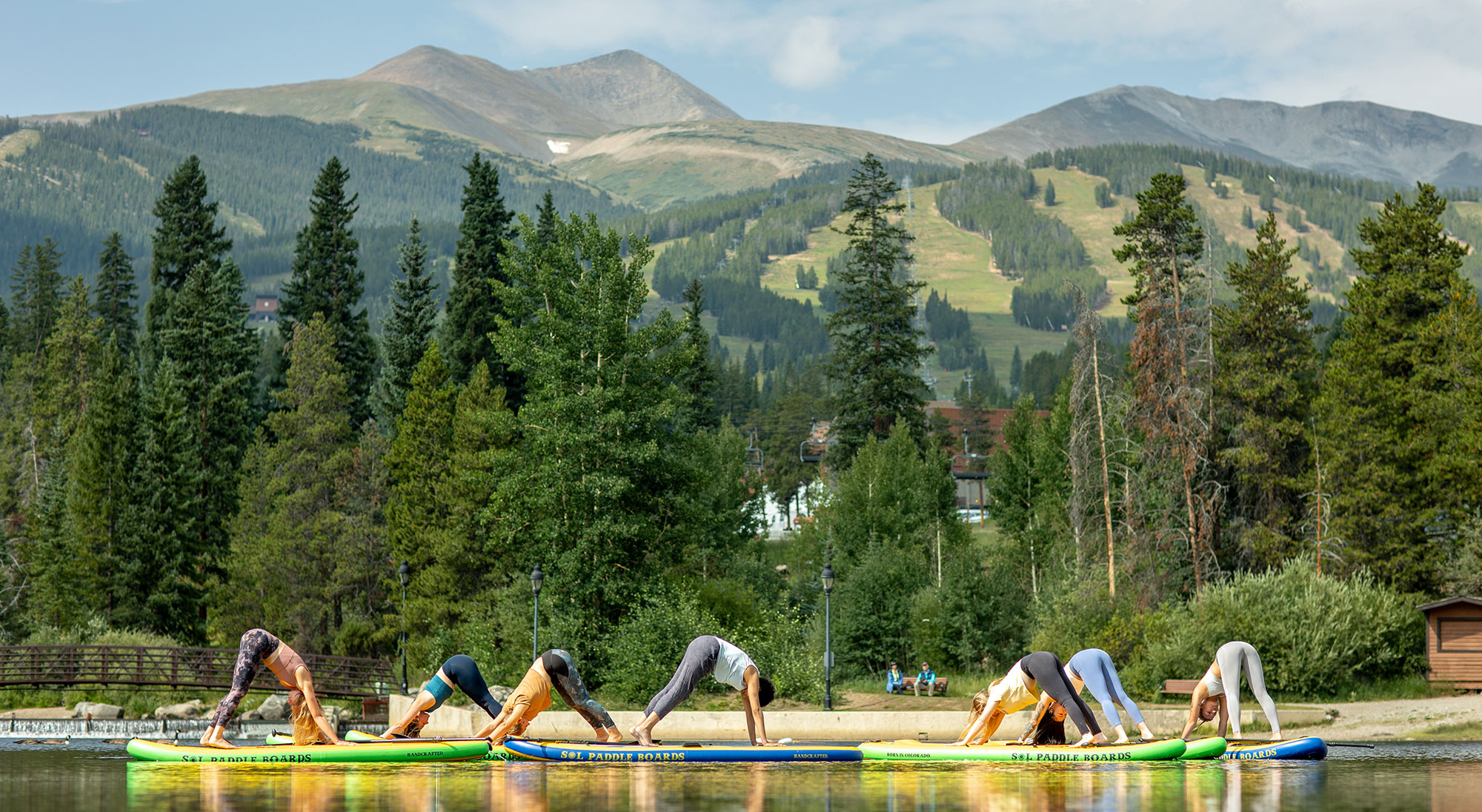 group of women do yoga poses on stand up paddleboards with mountain views